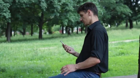 In the park a guy with a smartphone in his hand gets up and leaves Stock Footage 135238174