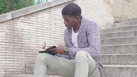 Park Note-Taking: Black Man Writes in Agenda on Park Stairs Stock Footage 265882652