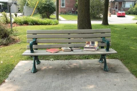 Park parkette bench with an assortment of books on it and no people, green Stock Photos