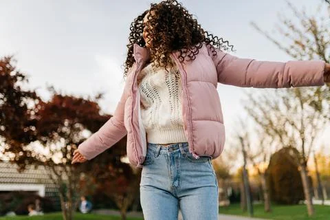 In the park in pink down jacket and jeans girl twirls her head spreading her Stock Photos