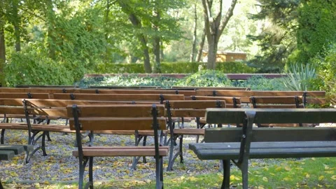 A park stage with rows of empty wooden benches set in a shaded area, surrou.. Video stock 293088403