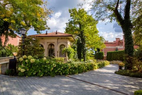 A park with a stone tile walk down the park with plants and a stone gazebo. Stock Photos