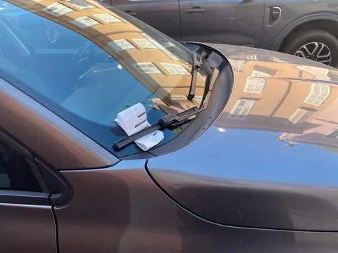 Parking ticket slipped under windshield wiper of parked car on sunny city s.. Stock Photos
