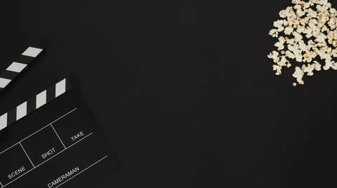 Part of black clapper board or movie slate and popcorn on black background. Stock Photos