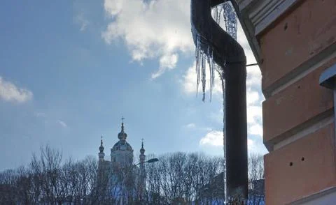Part of the old building with a drainpipe and icicles and St. Andrew's Church in 库存照片