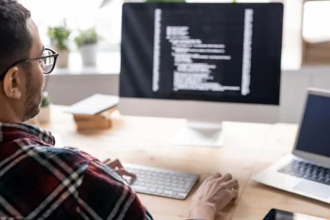 Part of young software developer sitting by table in front of computer monitor Stock Photos