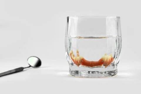 Partial denture inside glass next to dental mirror Stock Photos