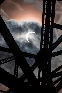 A partial eclipse is seen from underneath the bridge on a cloudy day Stock Photos