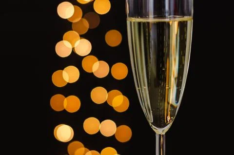 Partial focus of a glass of sparkling wine with golden bokeh lights on dark.. Stock Photos
