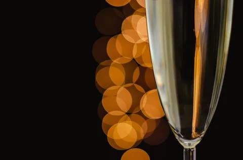 Partial focus of a glass of sparkling wine with golden bokeh lights on dark.. Stock Photos