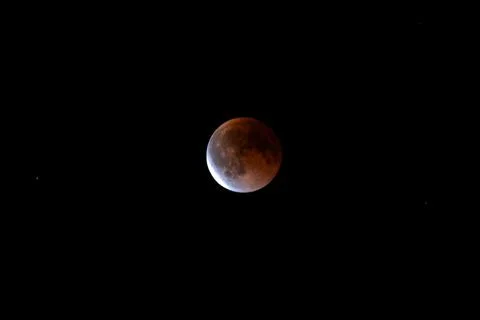 Partial lunar eclipse with copper moon and bright sunlit limb on black sky Stock Photos
