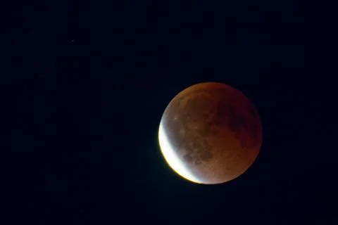 Partial lunar eclipse with reddish moon against dark night sky Stock Photos