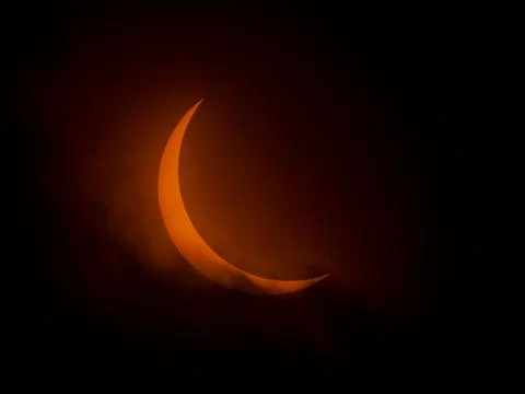 Partial solar eclipse as clouds move by orange crescent sun Stock Photos