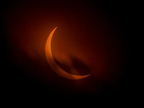 Partial solar eclipse as clouds streak by orange crescent sun Stock Photos