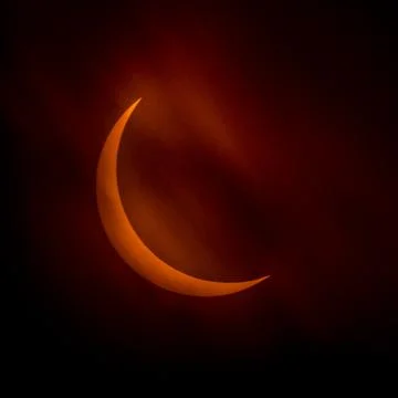 Partial solar eclipse as dark clouds streak by orange crescent sun Stock Photos