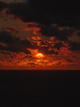 Partial solar eclipse during a dramatic sunset over the dark ocean water Stock Photos