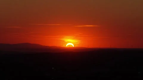 Partial solar eclipse during sunrise over hills with distant wind turbines Stock Footage 348363392