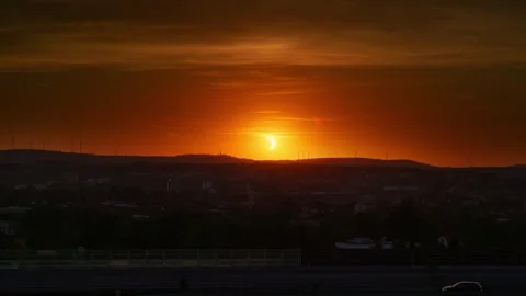 Partial Solar Eclipse Glowing Above Dark Horizon in Orange Evening Sky Stock Footage 342998221