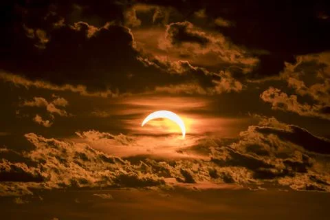 Partial solar eclipse with glowing sun and dark clouds at sunset time Stock Photos