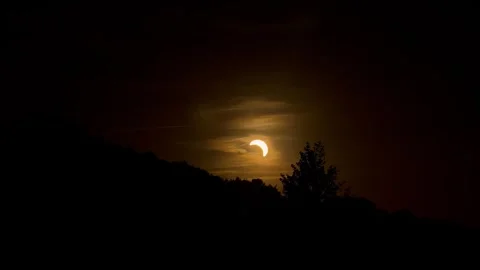 Partial solar eclipse glows as thin bright crescent through hazy smoky orange Stock Footage 343401993