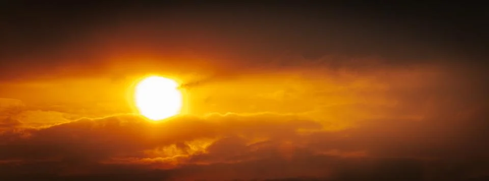 A partial solar eclipse glows through dramatic red-orange clouds Stock Photos
