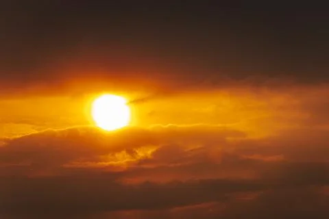 A partial solar eclipse glows through dramatic red-orange clouds Stock Photos
