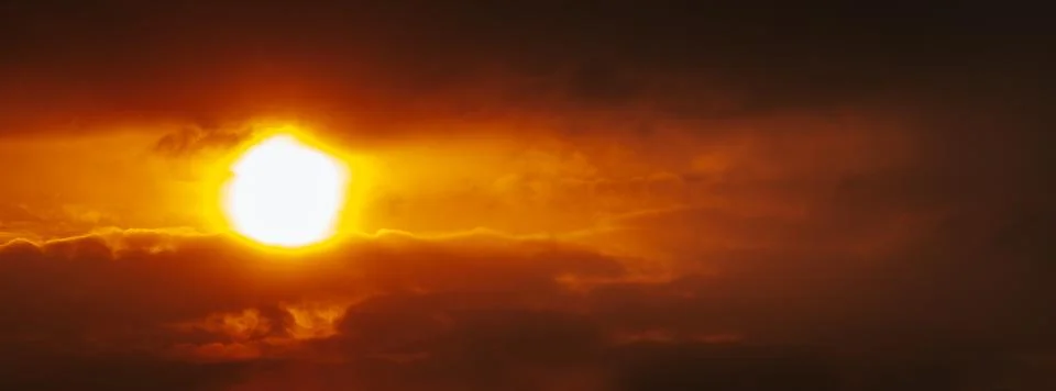 A partial solar eclipse glows through dramatic red-orange clouds Stock Photos