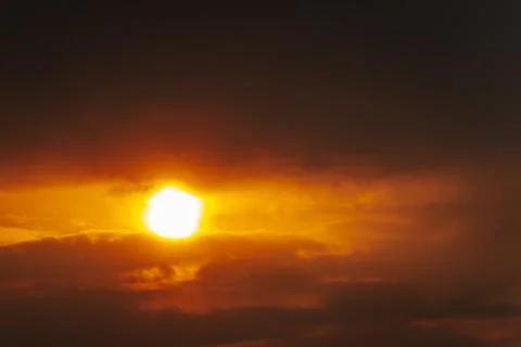 A partial solar eclipse glows through dramatic red-orange clouds Stock Photos