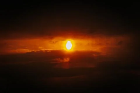 A partial solar eclipse glows through dramatic red-orange clouds Stock Photos
