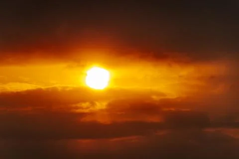 A partial solar eclipse glows through dramatic red-orange clouds Stock Photos