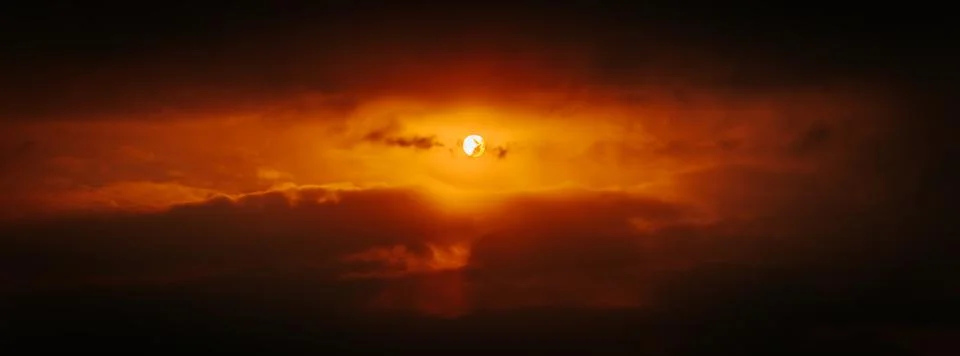 A partial solar eclipse glows through dramatic red-orange clouds Stock Photos