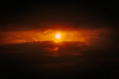 A partial solar eclipse glows through dramatic red-orange clouds Stock Photos