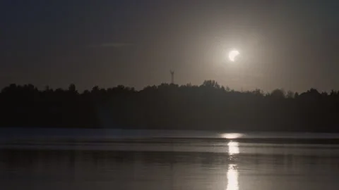 Partial solar eclipse over calm lake with reflection Stock Footage 344052604
