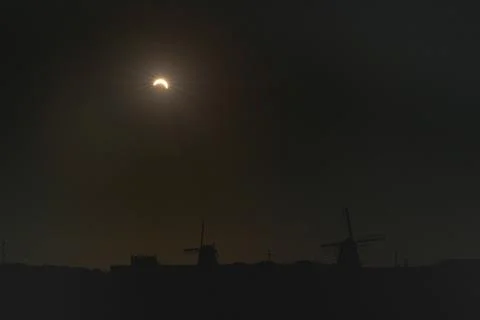 Partial solar eclipse over silhouetted windmills at dusk with dark evening sky Stock Photos