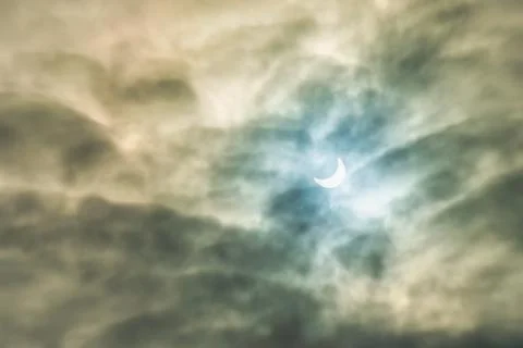 Partial solar eclipse passing behind the clouds. Stock Photos