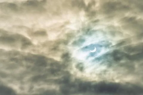 Partial solar eclipse passing behind the clouds. Stock Photos