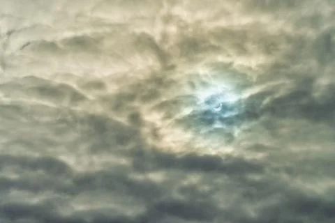 Partial solar eclipse passing behind the clouds. Stock Photos