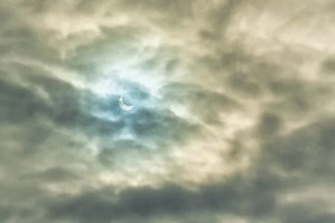 Partial solar eclipse passing behind the clouds. Stock Photos