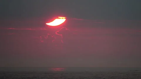 Partial solar eclipse with red-rimmed cumulous clouds at dawn over Stock Footage 155669883