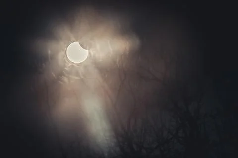 A partial solar eclipse in the sky over Latvia with rays piercing through clouds Stock Photos