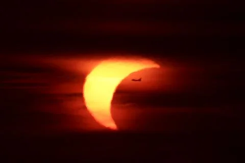 Partial solar eclipse at sunset with an airplane silhouette transit Stock Photos