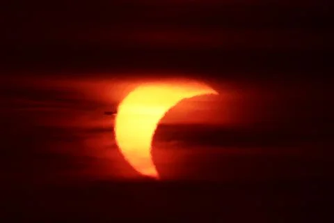 Partial solar eclipse at sunset with an airplane silhouette transit Stock Photos