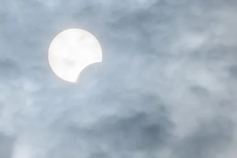 Partial sun eclipse behind clouds Stockfoto's