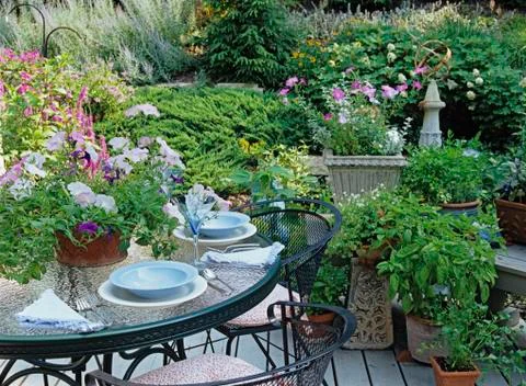 Partial view of table set with dishes on deck, lots of potted plants and flowers Stock Photos