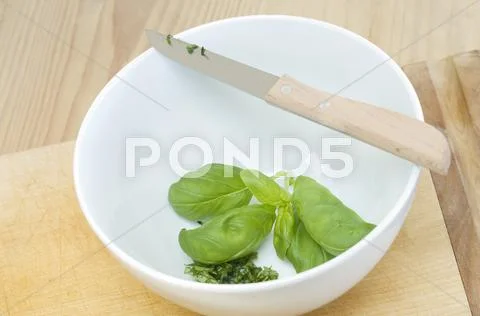 Partially chopped basil in a bowl with a knife Stock-Fotos