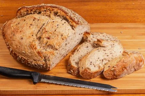Partially cut artisan grain bread on cutting board with knife Stock Photos