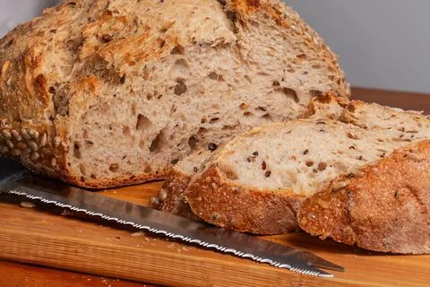 Partially cut artisan grain bread with serrated knife close-up Stock Photos