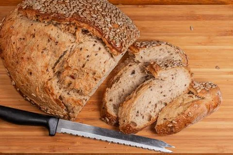 Partially cut artisan grain bread on cutting board with knife Stock Photos