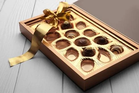Partially empty box of chocolate candies on white wooden table Stock Photos
