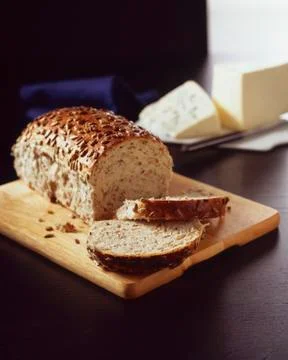 Partially Sliced Loaf of Multi Grain Bread on a Cutting Board; Cheese Stock Photos